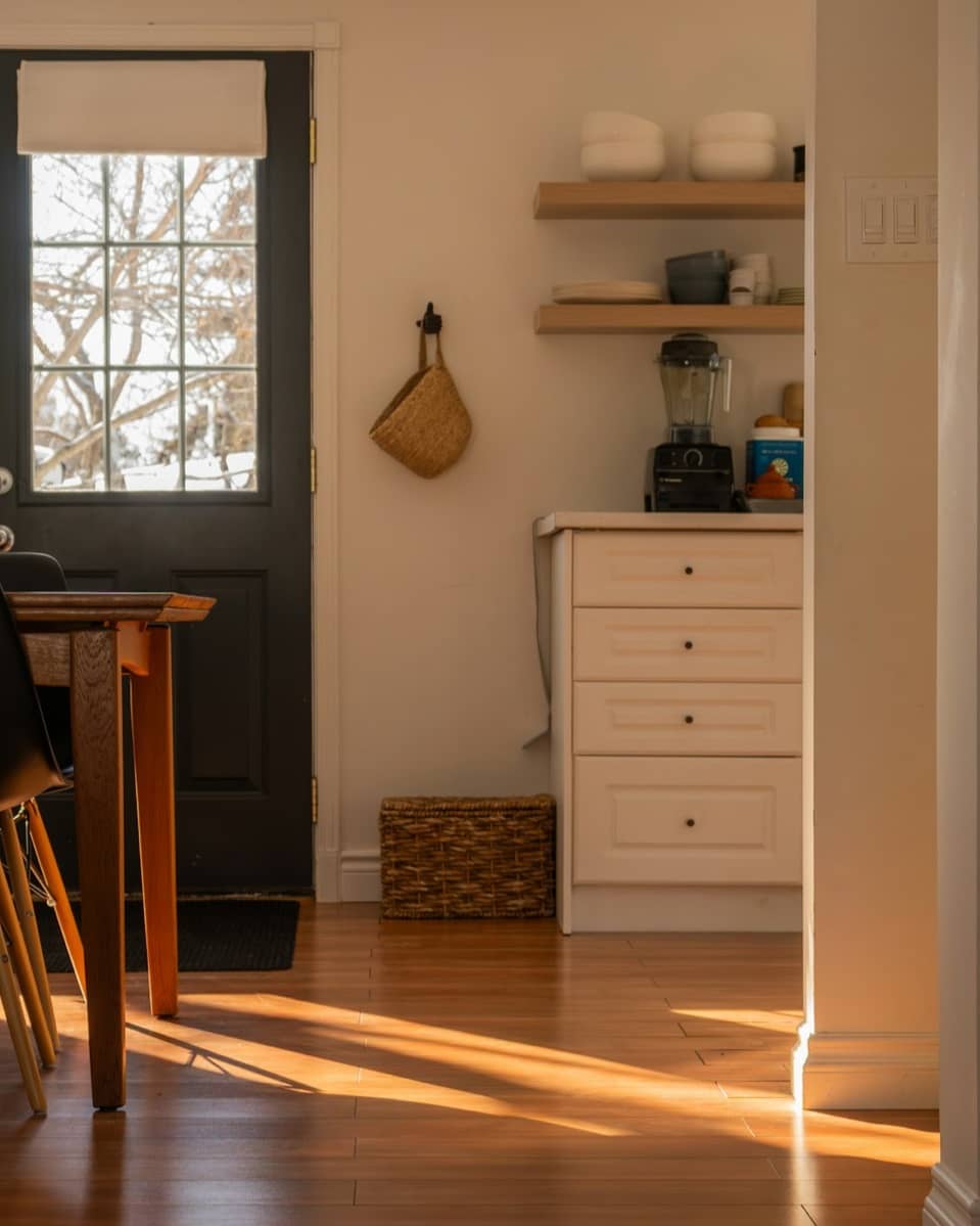 Sunlight streaming across a modest kitchen and dining nook, with a back door and wooden floors.