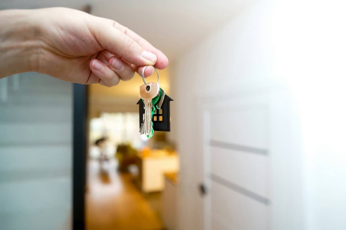 A hand holding out a set of keys on a little house-shaped keychain in a bright entryway.