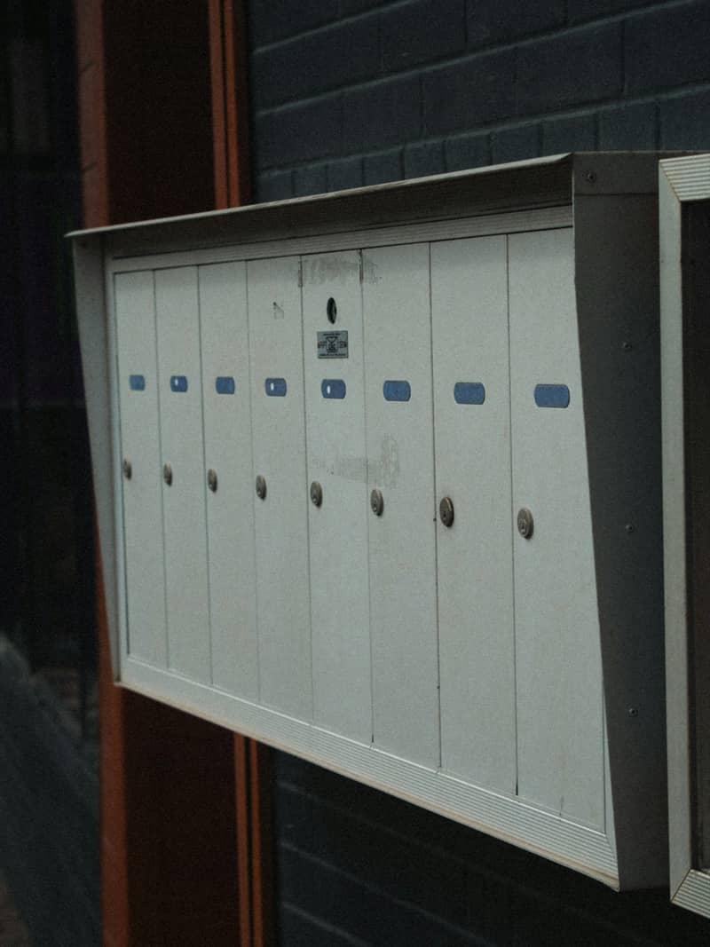 A bank of numbered white unit mailboxes on a dark brick wall.